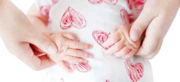 a woman holding her baby's hands with hearts drawn on it
