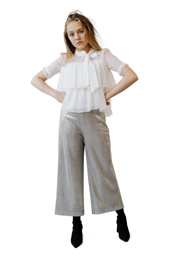 a woman wearing a white top and silver pants